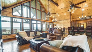 A spacious living room with leather furniture, large windows, and a high ceiling fan. - Broken Bow Cabin w/ Game Room & Private Hot Tub! (Broken Bow)