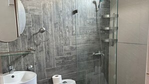 Ein modernes Badezimmer mit Holzwand, einer Duschkabine aus Glas, einer weißen Toilette und einem hölzernen Waschtisch.