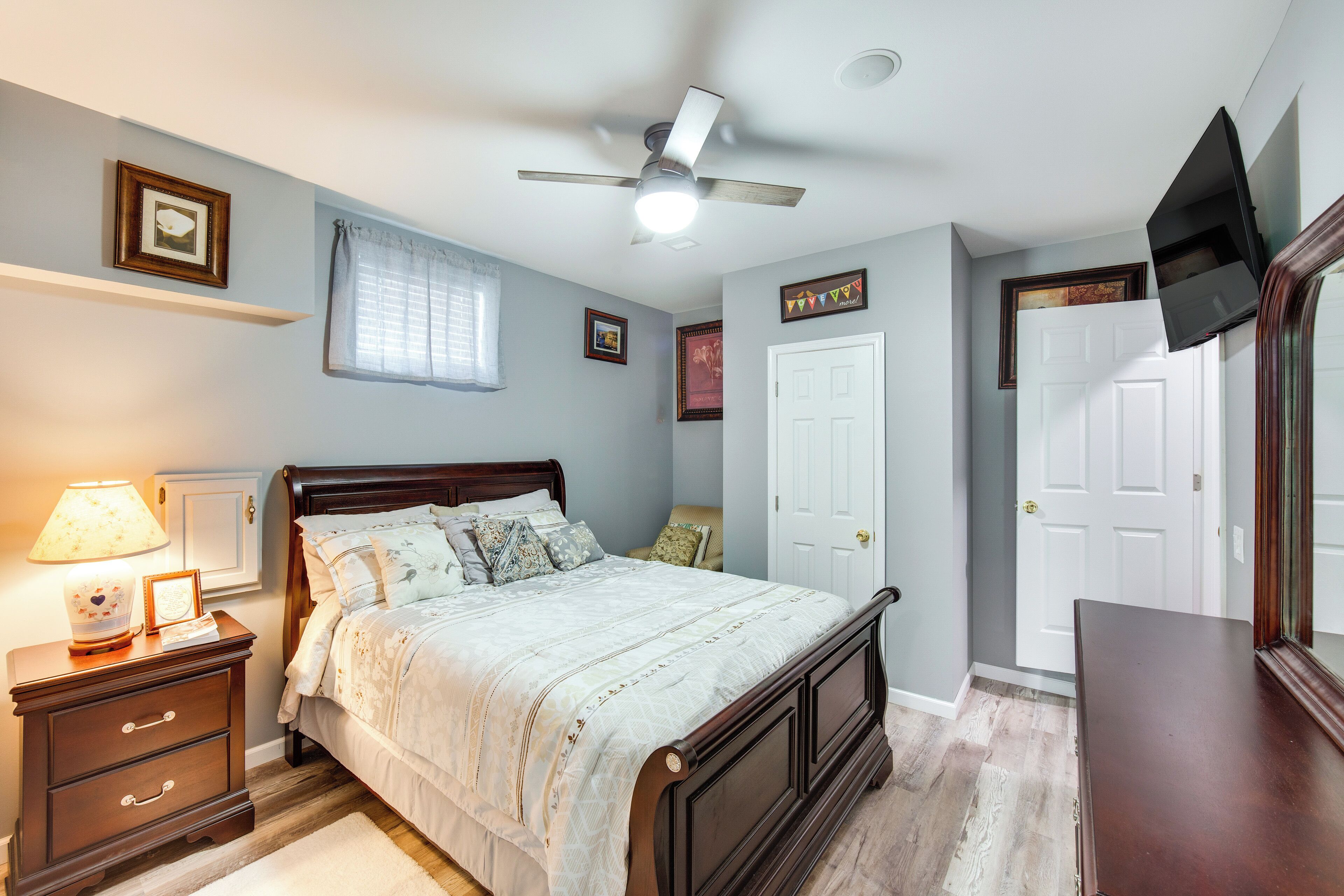 Ein Schlafzimmer mit Bett, Nachttisch, Lampe, Deckenventilator und einem an der Wand befestigten Fernseher.