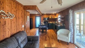 Ein gemütliches Wohnzimmer mit einer Couch und einem Sessel, ein Essbereich mit Tisch und Stühlen sowie eine Küche mit Holzwänden und modernen Geräten.