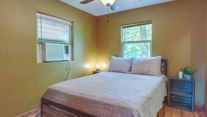 Ein Schlafzimmer mit einem hölzernen Bett, zwei Fenstern, einem Deckenventilator und einem Nachttisch mit einer Lampe.