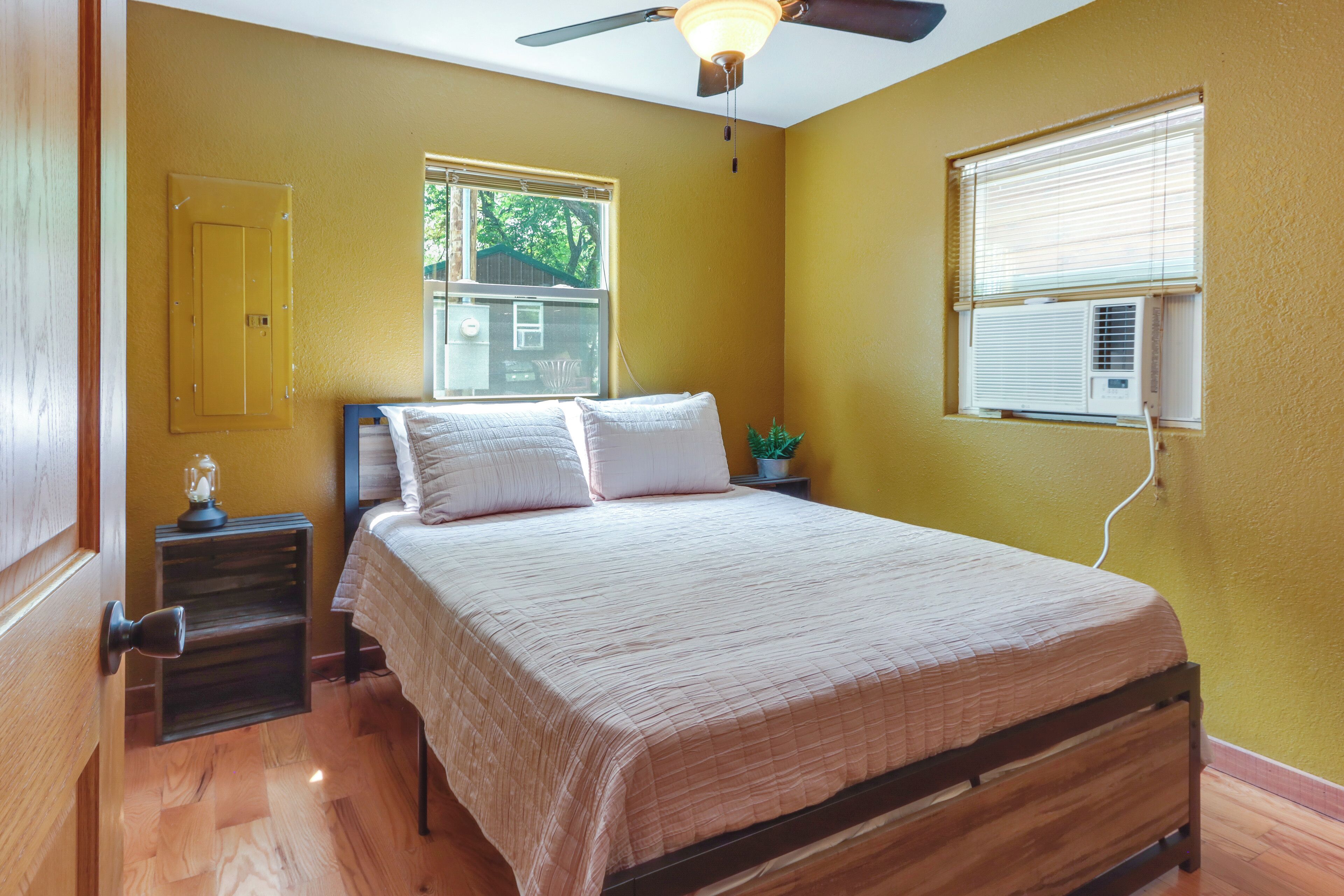 A bedroom with a bed, a nightstand, a ceiling fan, a window with blinds, and an air conditioning unit.