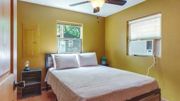A bedroom with a bed, a nightstand, a ceiling fan, a window with blinds, and an air conditioning unit.