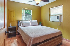 Ein Schlafzimmer mit Bett, Nachttisch, Deckenventilator, Fenster mit Jalousien und Klimaanlage.