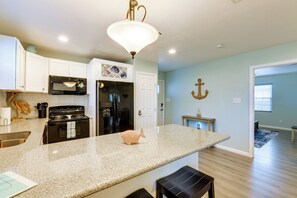A kitchen with white cabinets, a granite countertop, a fish-shaped soap holder, and a hanging light fixture. - Relax at Heron Bay Cottage in Rockport, Texas! (Rockport)