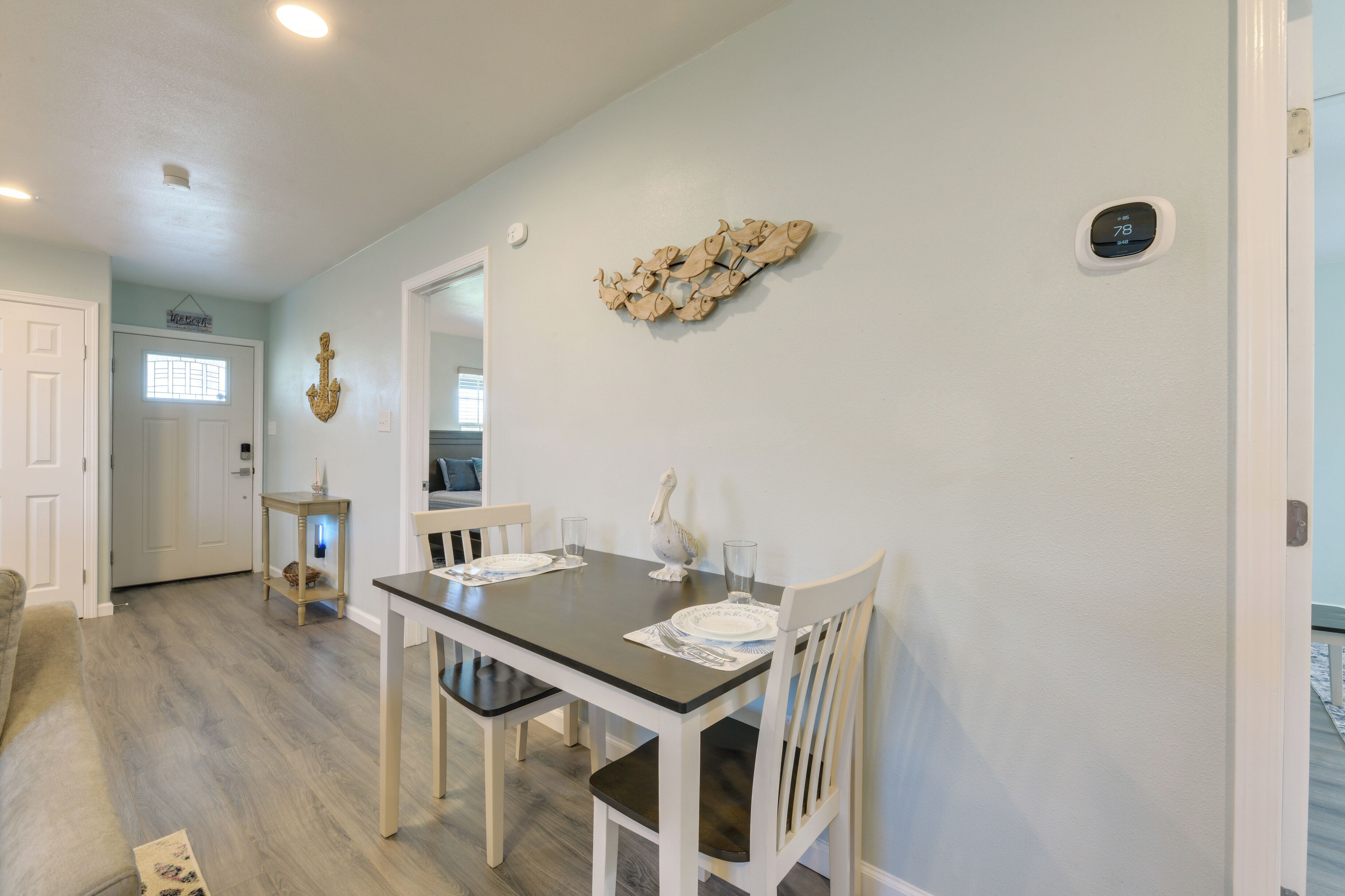 A dining area with a table set for two, a decorative wall piece, and a thermostat on the wall.