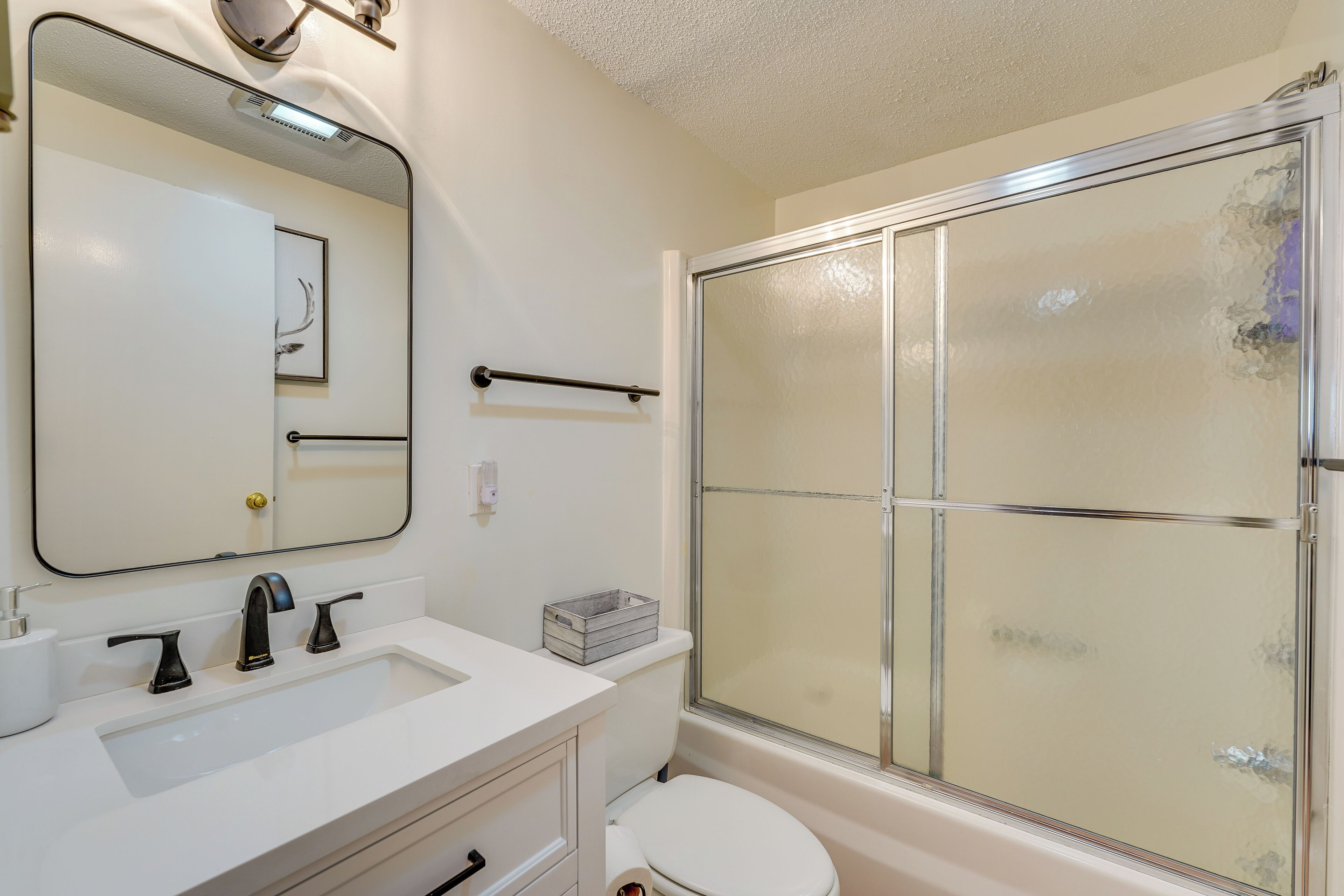 Une salle de bain avec un lavabo blanc, un miroir, des toilettes et une douche à parois de verre.