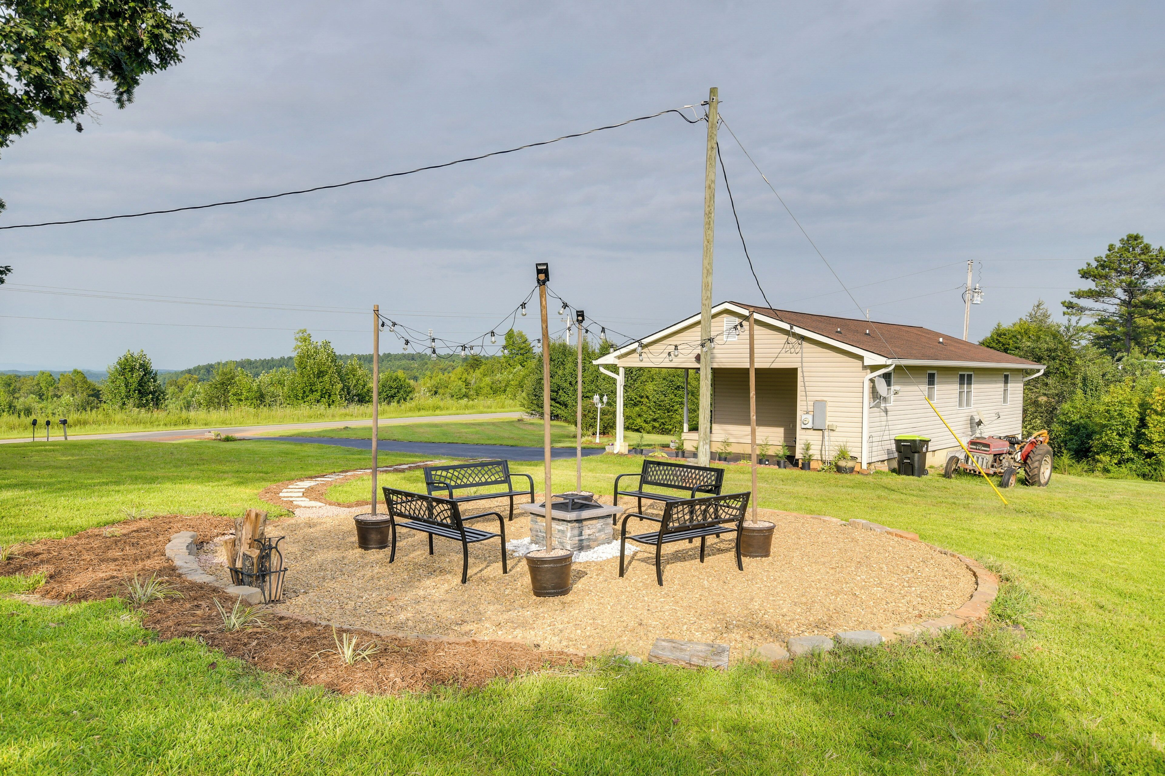 A covered outdoor seating area with a fire pit, surrounded by a grassy field and a house in the background.