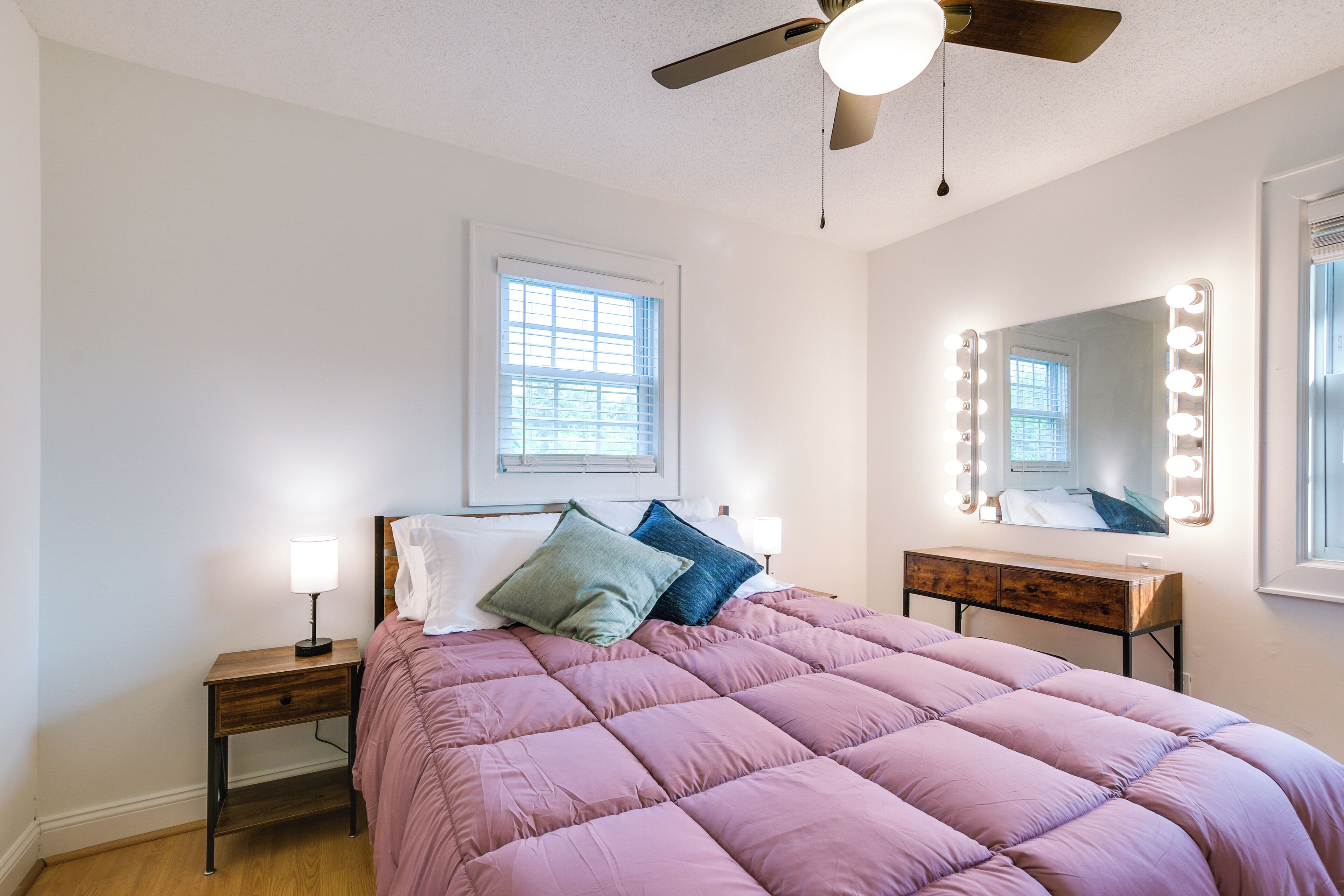 Een slaapkamer met een bed, nachtkastje, dressoir, plafondventilator en een raam.