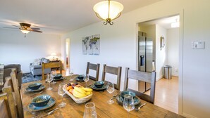 Comedor con mesa de madera dispuesta para seis comensales, rodeada de sillas, una obra de arte con un globo terráqueo en la pared y un ventilador de techo.