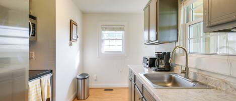 A modern kitchen with stainless steel appliances, a marble countertop, and a window with blinds.