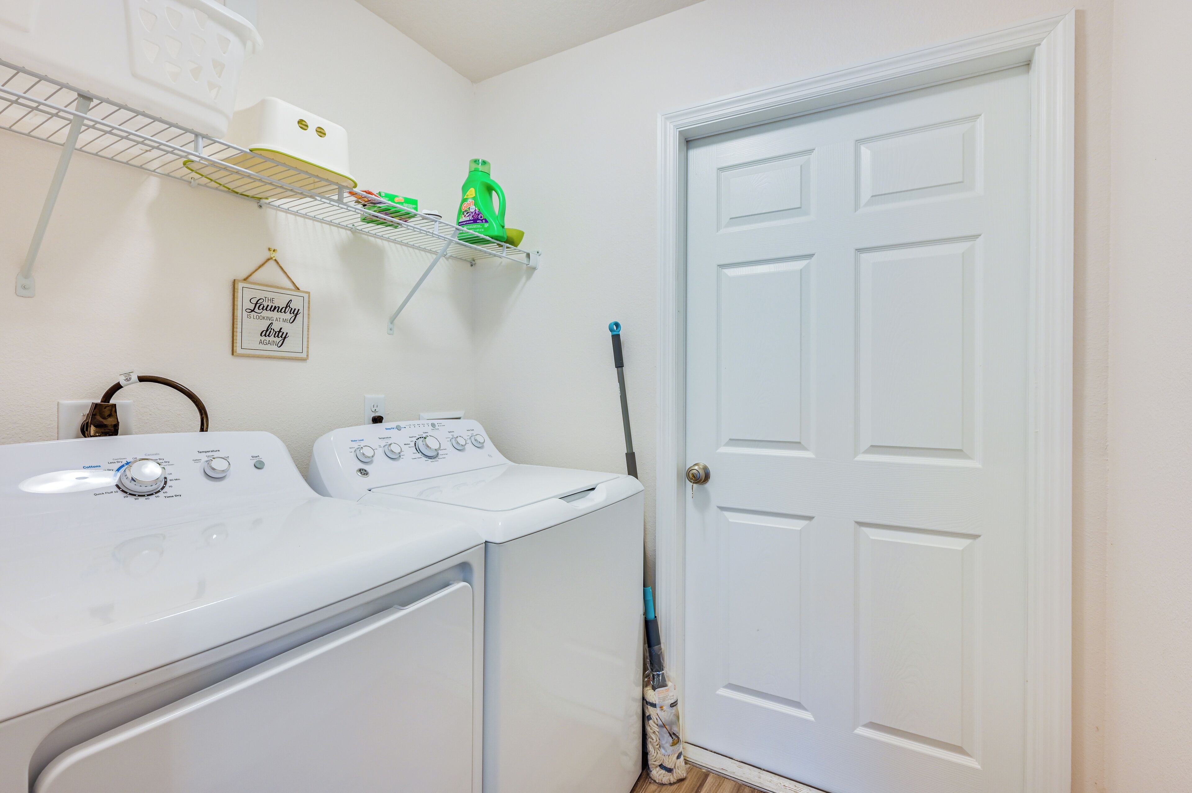 A laundry area with a washing machine, dryer, and a mop leaning against the wall.
