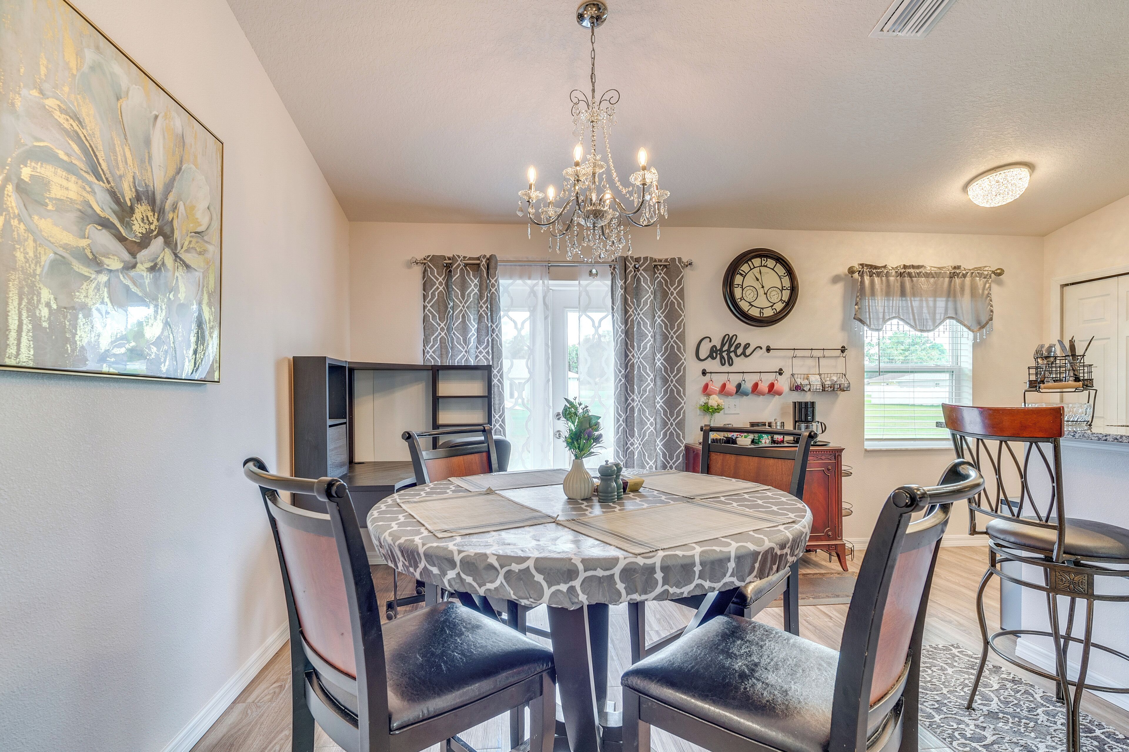 A dining area with a round table, chairs, a chandelier, and a clock on the wall.