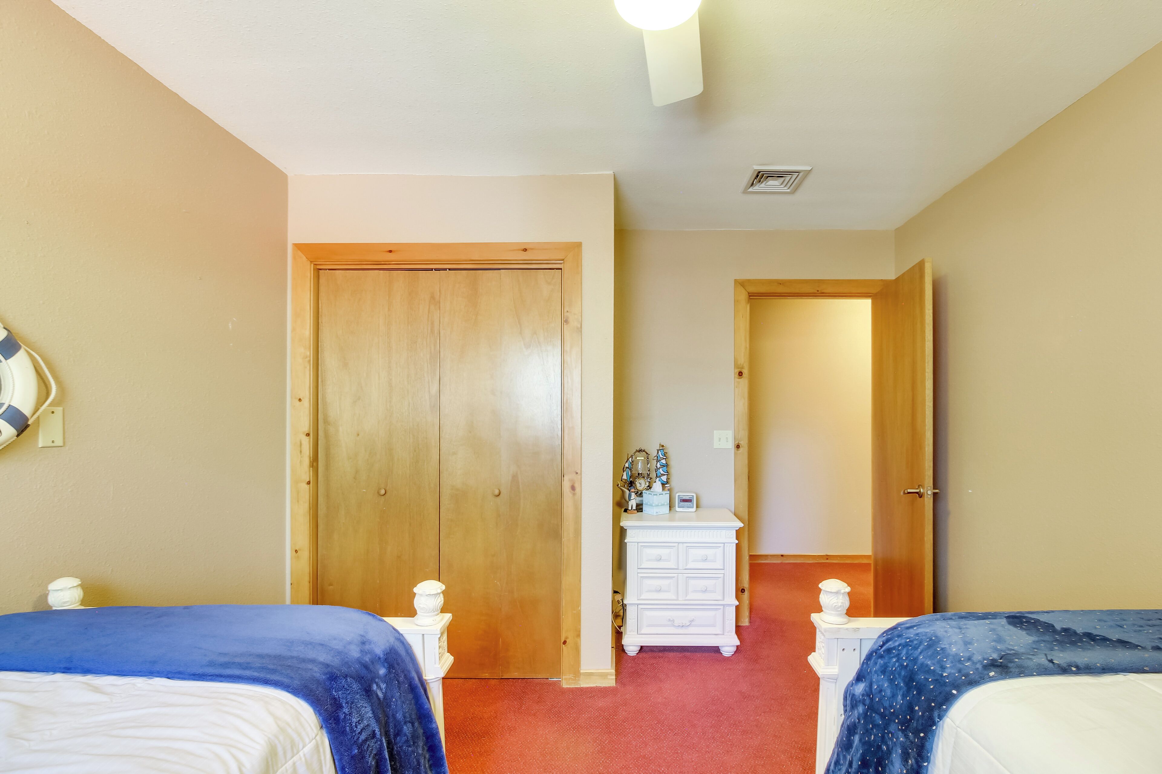 Une chambre avec deux lits, une porte en bois, une commode blanche et un tapis rouge.