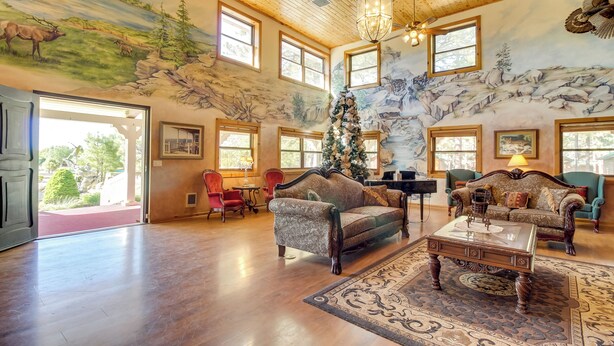 Ein großzügiger Wohnraum mit hohen Decken, Holzbalken und einem Wandgemälde einer Berglandschaft. Es gibt zwei Sofas, einen Couchtisch und einen Weihnachtsbaum.