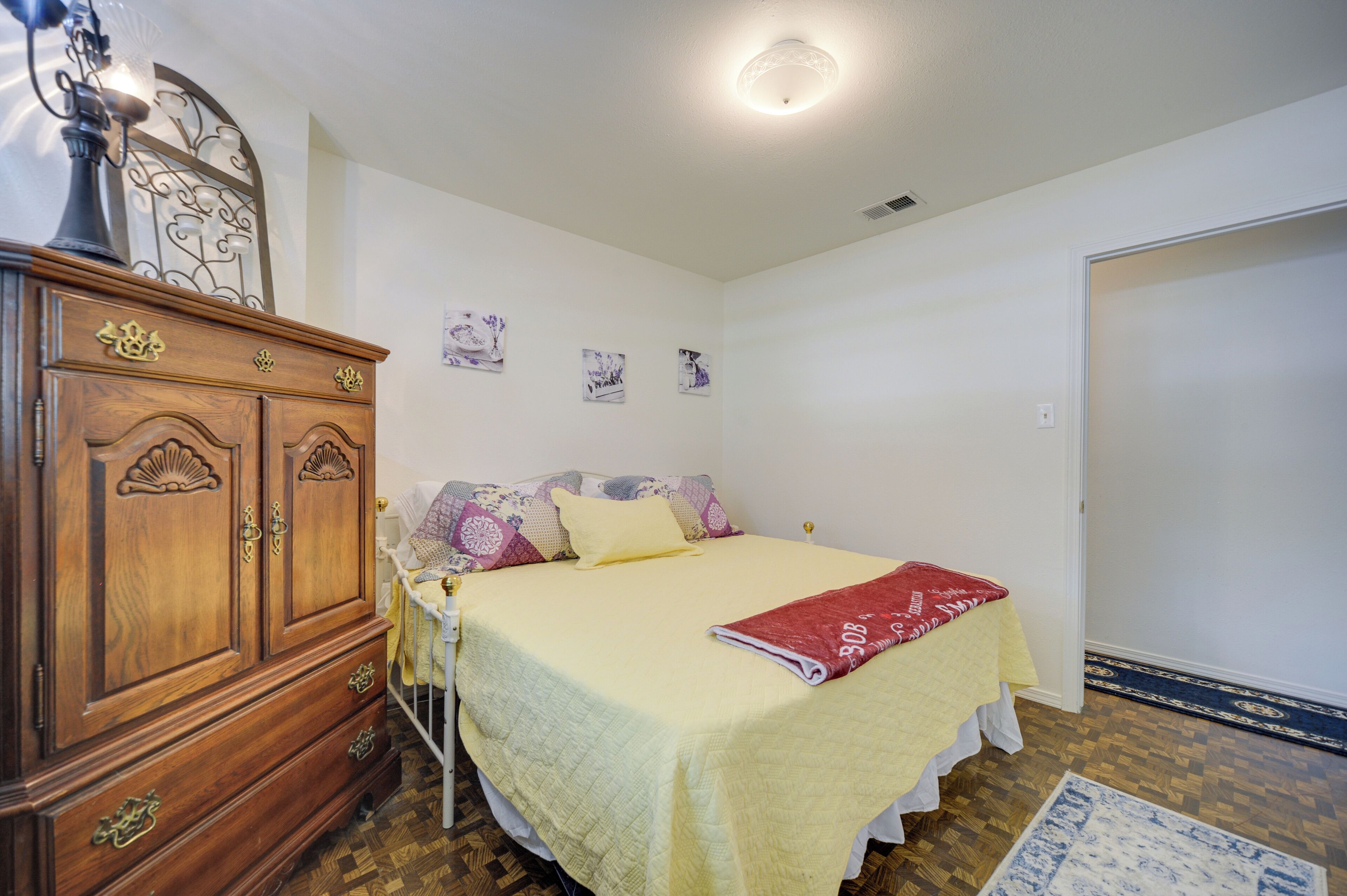 A bedroom with a bed, a wooden dresser, a nightstand, and a door.