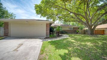Enjoy a peaceful stay in this single-story house with a spacious garage and serene front yard featuring lush plants and a mature tree.