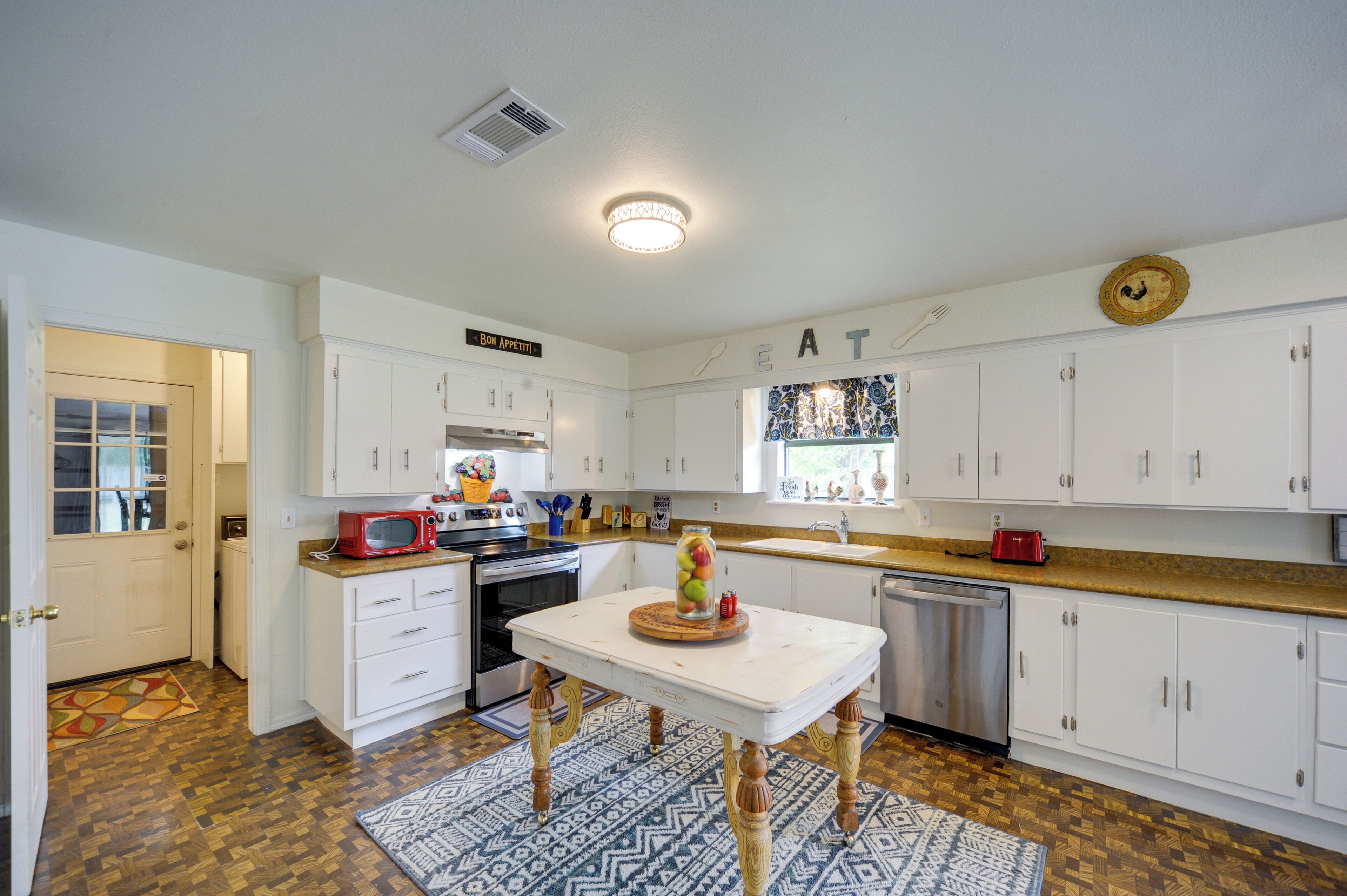 A modern kitchen with white cabinets, a wooden floor, and a central island with a fruit bowl.