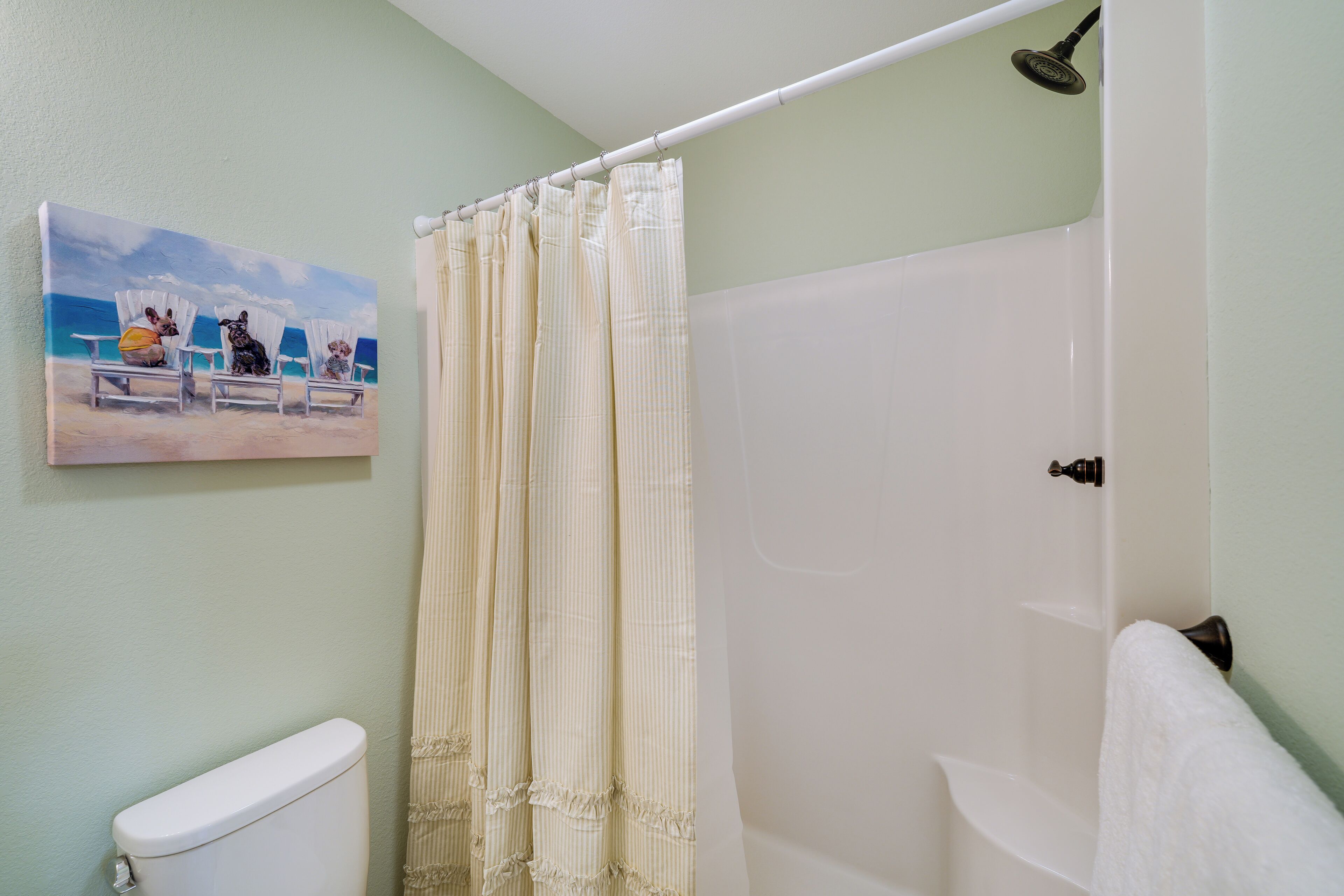 Une salle de bain avec un rideau de douche, des toilettes et un tableau représentant des chaises de plage.