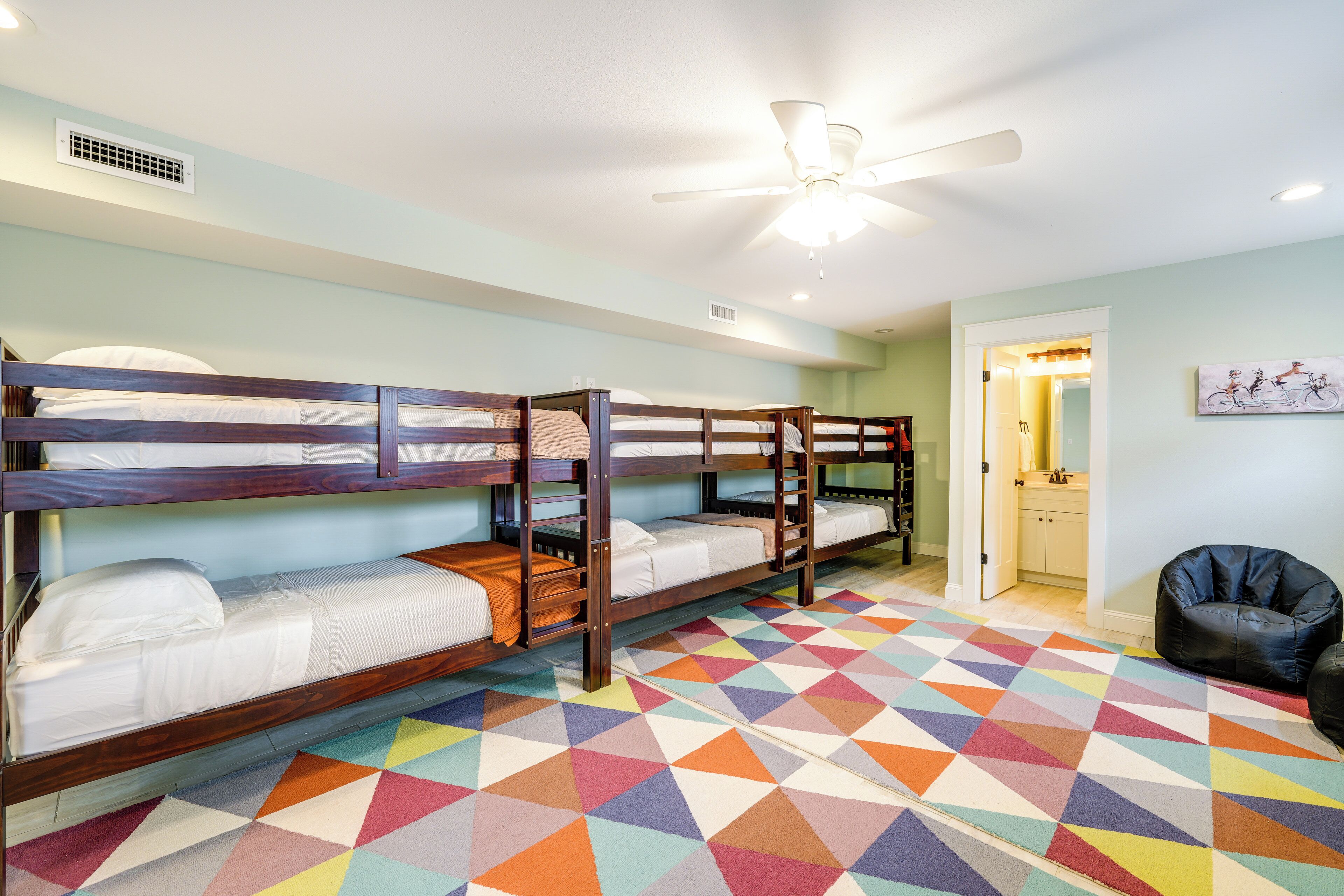 Ein Zimmer mit Etagenbetten, einem Deckenventilator und einem farbenfrohen Teppich mit geometrischem Muster.