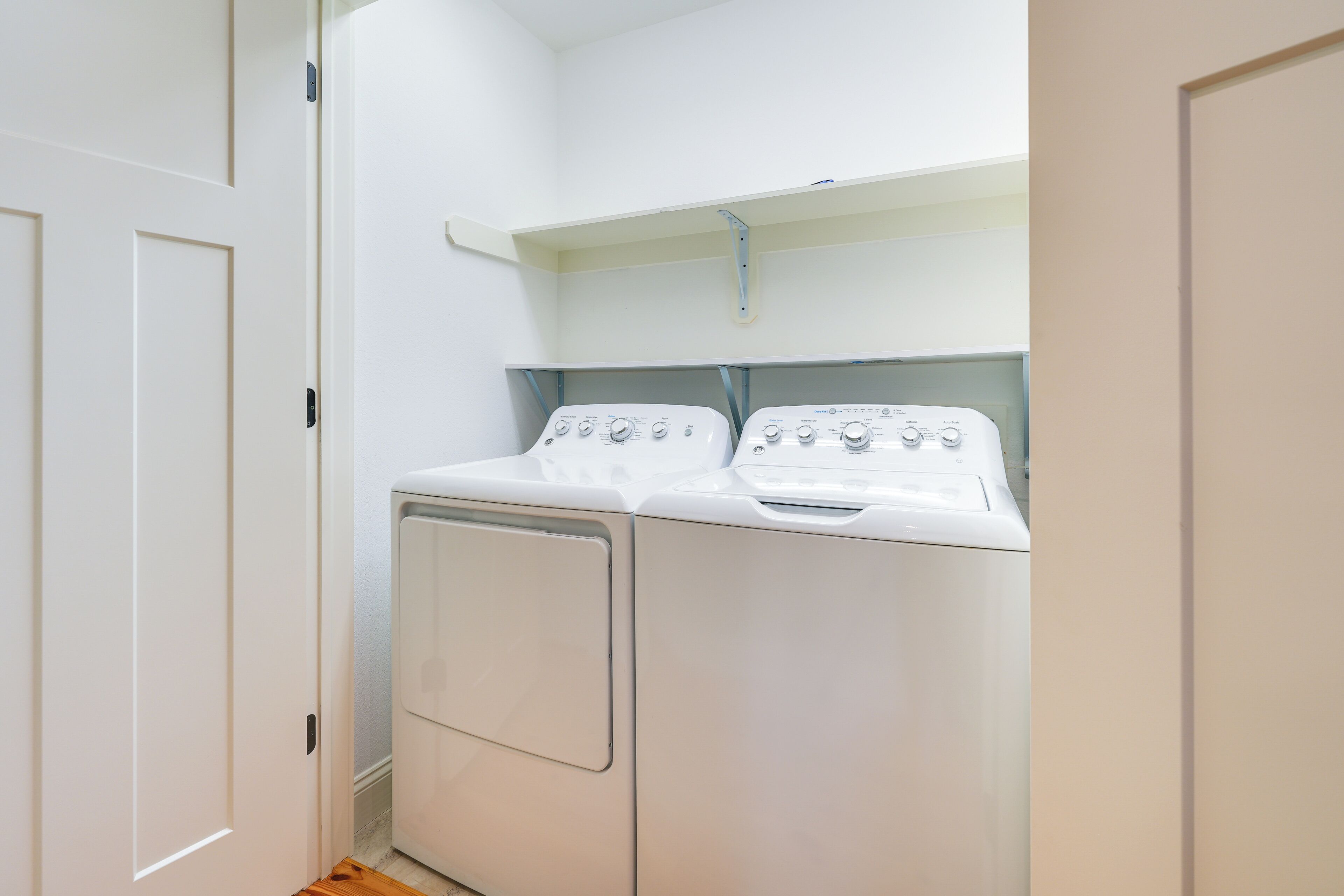 A laundry room with two white washing machines and a shelf above them.