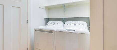 A laundry room with two white washing machines and a shelf above them.
