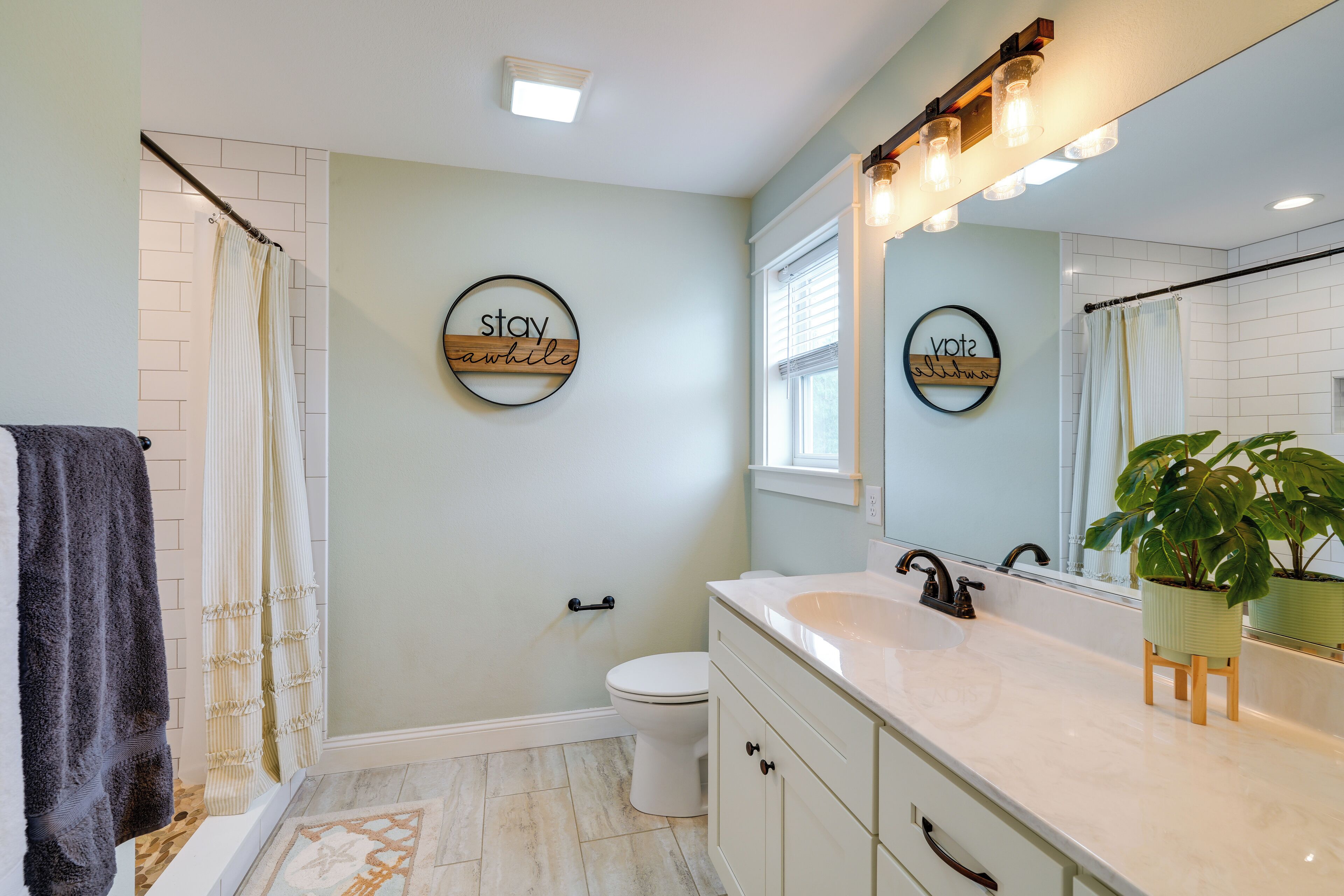 A bathroom with a white toilet, a sink with a mirror above it, and a shower curtain. There are two wall-mounted signs with text.