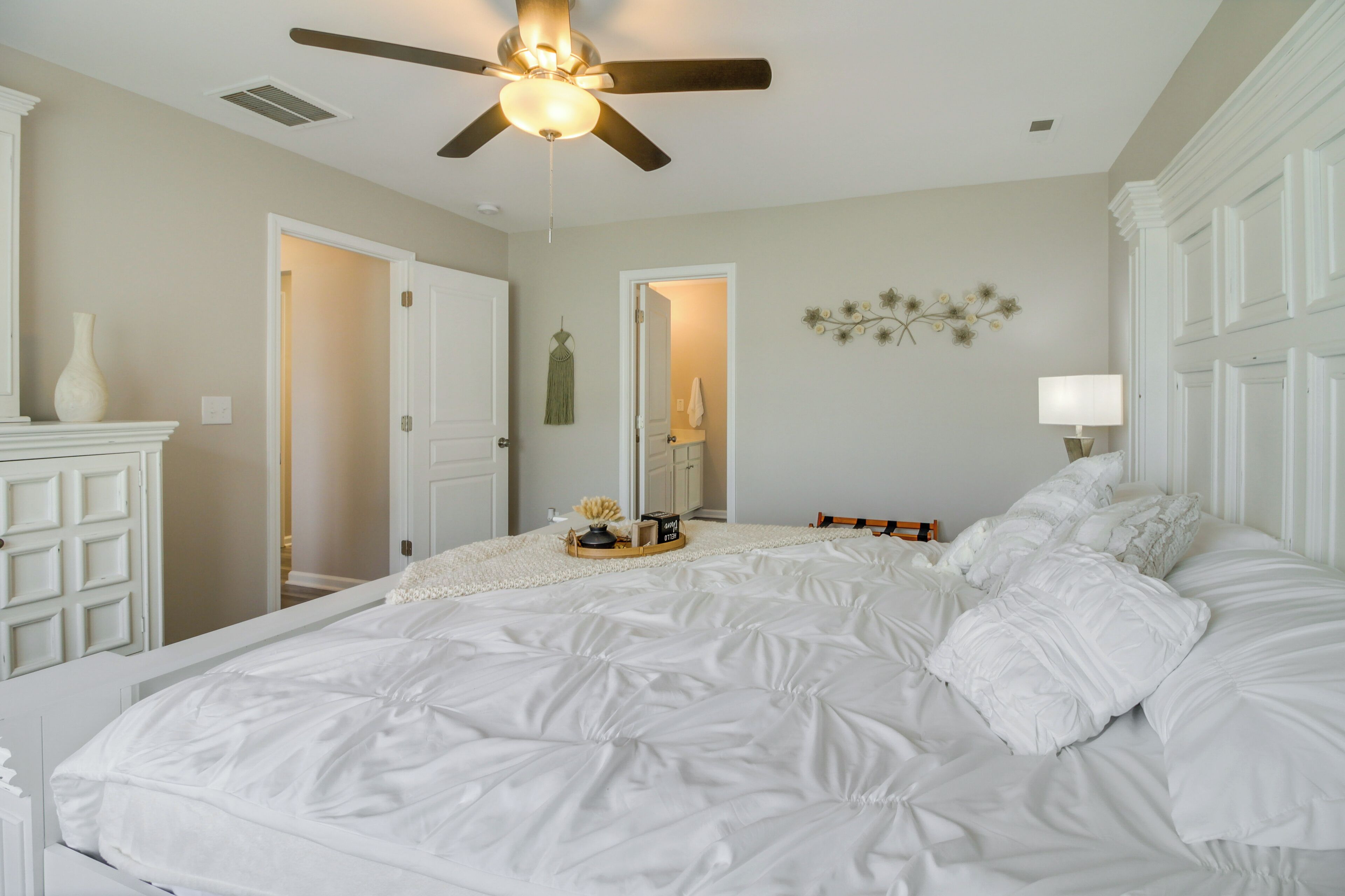 A bedroom with a bed, a ceiling fan, a dresser, and a door leading to another room.