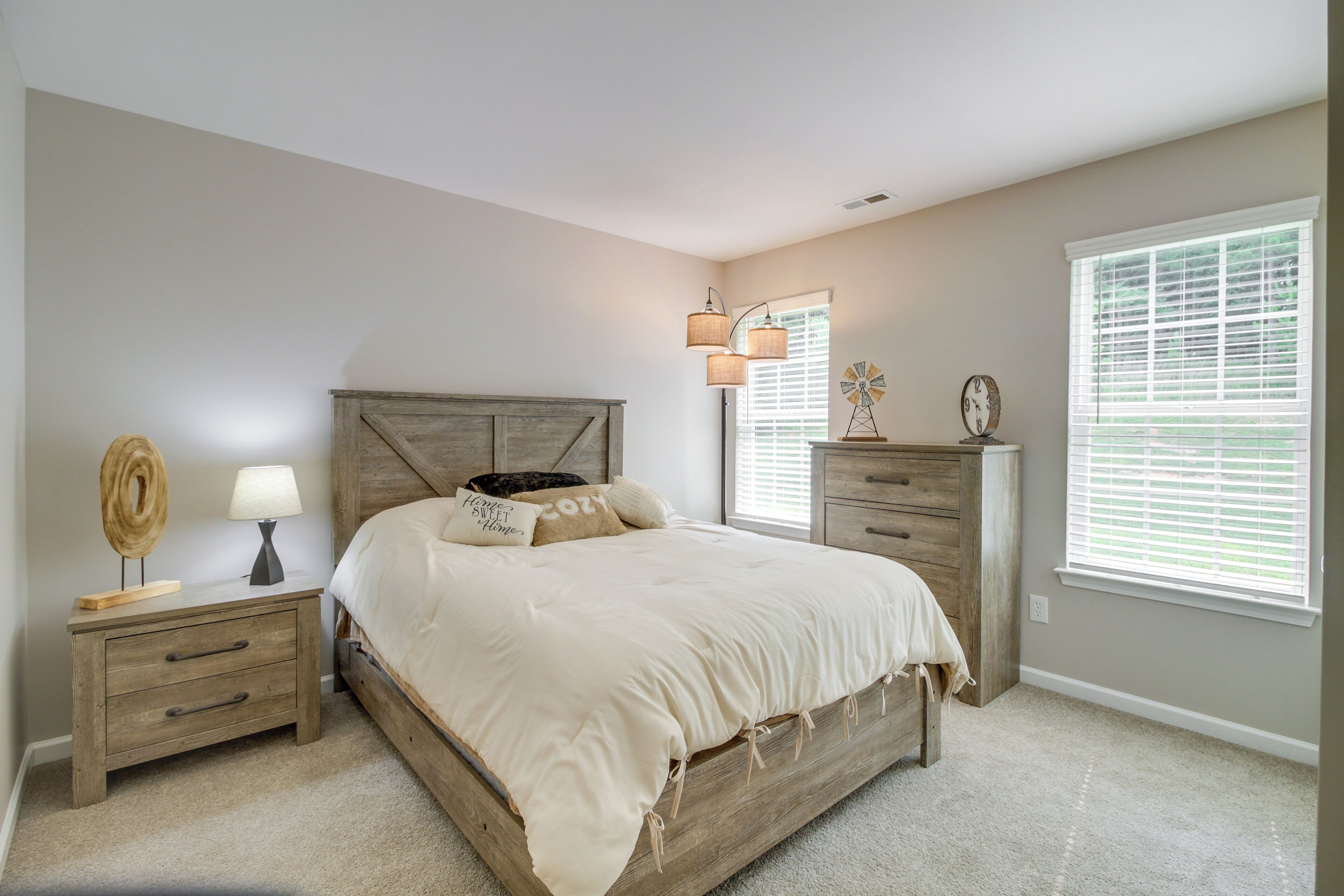 A bedroom with a wooden bed, bedside tables, a lamp, and a window with blinds.