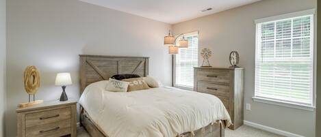 A bedroom with a wooden bed, bedside tables, a lamp, and a window with blinds.