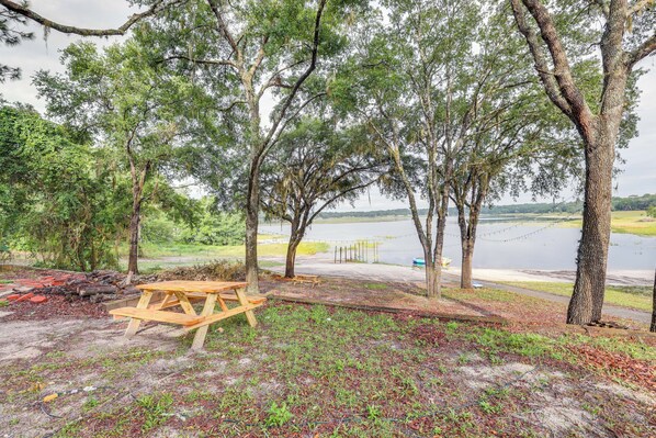 A picnic area with a wooden table and benches, surrounded by trees and a view of a lake.