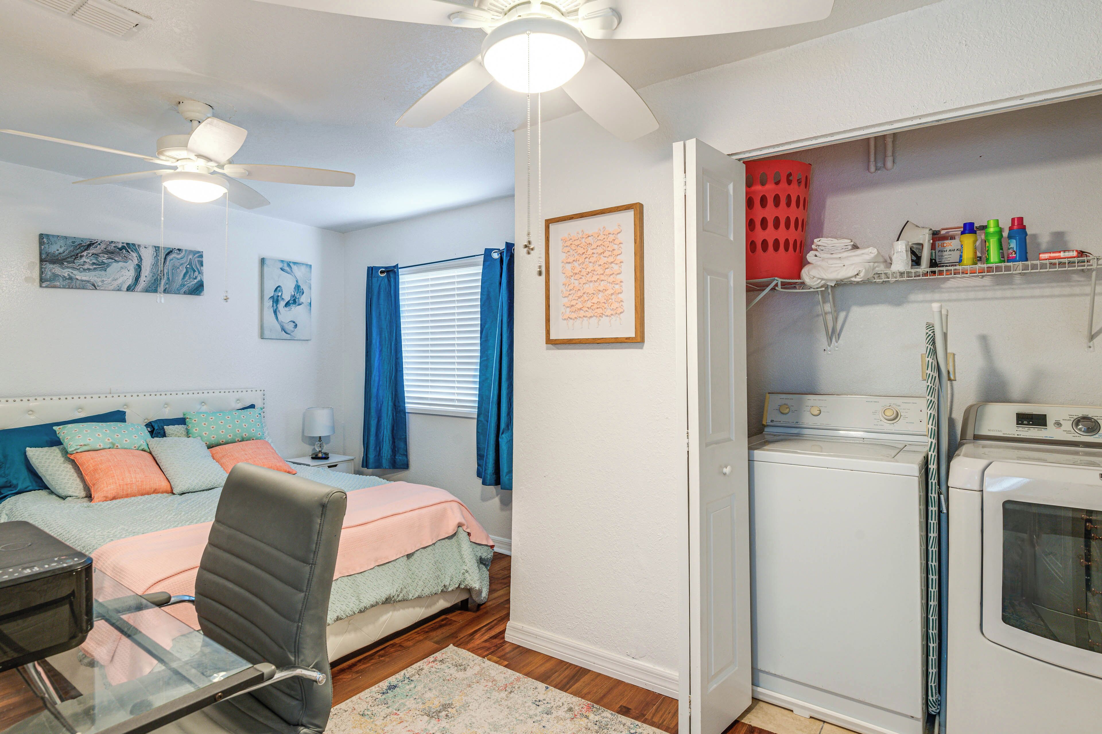 Un dormitorio con cama, escritorio, silla, ventilador de techo y zona de lavandería con lavadora y secadora.