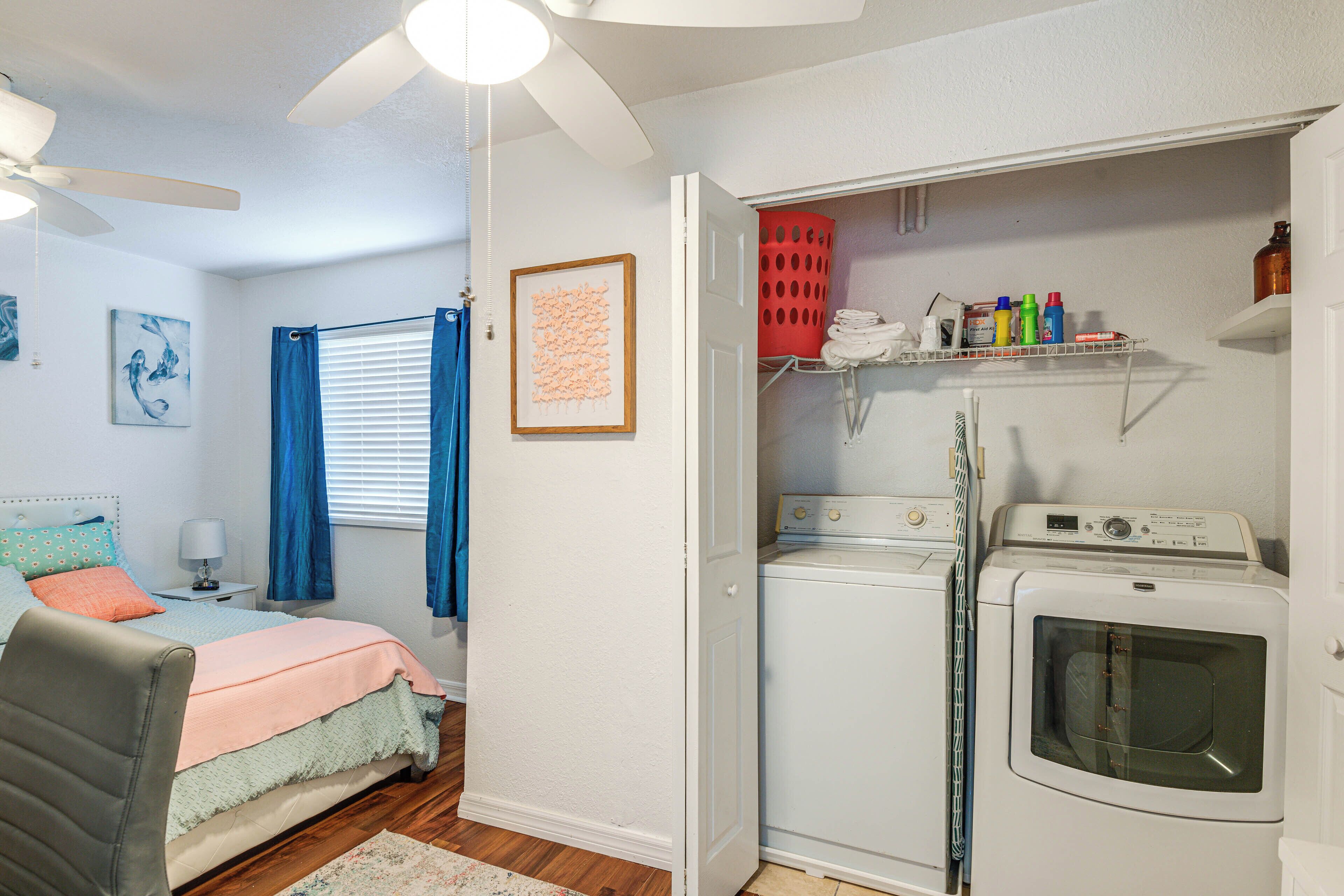 Un dormitorio compacto con cama, ventilador de techo y zona de lavandería con lavadora y tendedero.