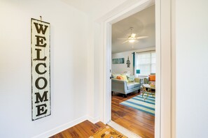 A hallway with a 'WELCOME' sign, a ceiling fan, and a view into a living room with a sofa, coffee table, and a rug. - Lakefront Keystone Heights Home w/ Boat Ramp! (Keystone Heights)