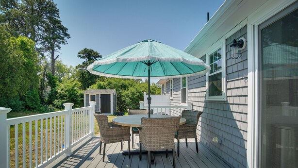 A deck with a table and chairs, a green umbrella, and a white railing. - Newly Renovated Dennis Port Home: Close to Beaches (Dennis Port)