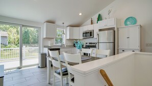 A modern kitchen with white cabinetry, stainless steel appliances, and a dining area with white chairs. - Newly Renovated Dennis Port Home: Close to Beaches (Dennis Port)