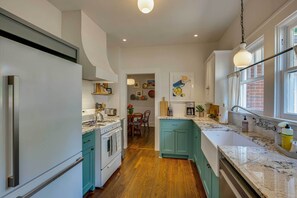 A kitchen with white cabinets, teal accents, a large island with a sink, and a view to the dining area. - Walk to Bergfeld Park: 1928 Azalea District Home (Tyler)