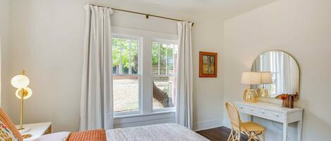 Un dormitorio con cama, escritorio, silla, lámpara, ventana con cortinas y ventilador de techo.