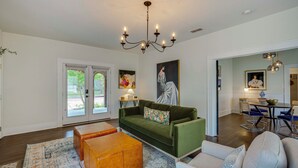 A living room with a green sofa, wooden coffee table, and a chandelier. - Walk to Bergfeld Park: 1928 Azalea District Home (Tyler)