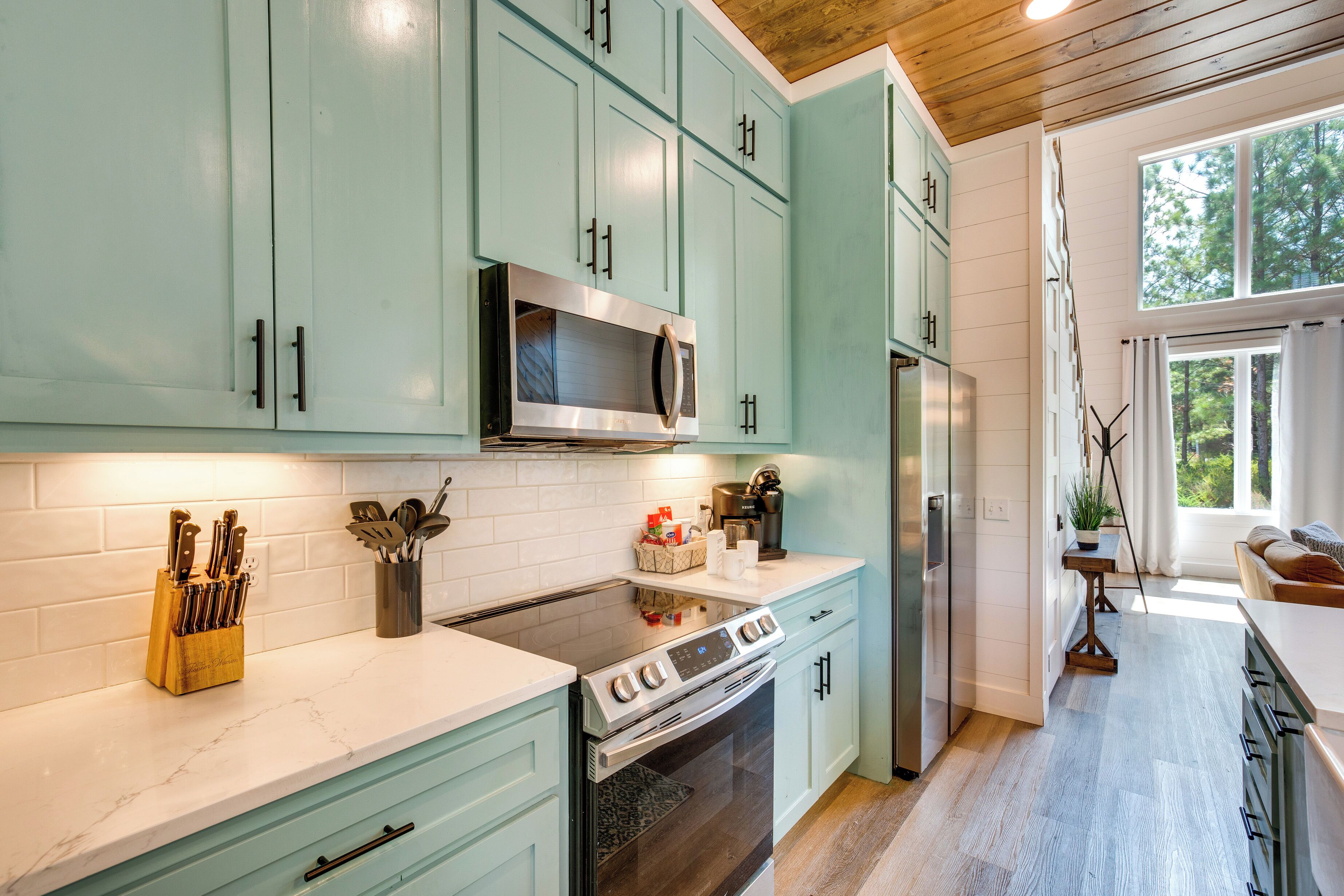 A modern kitchen with teal cabinets, stainless steel appliances, and a white countertop.