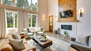 Ein geräumiges Wohnzimmer mit großem Fenster, Kamin und Wandfernseher.