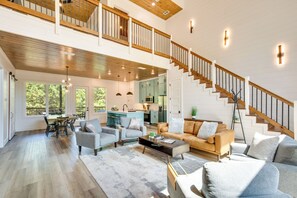 Un vaste espace de vie doté d’un haut plafond, d’un escalier en bois et offrant une vue sur la cuisine et la salle à manger.