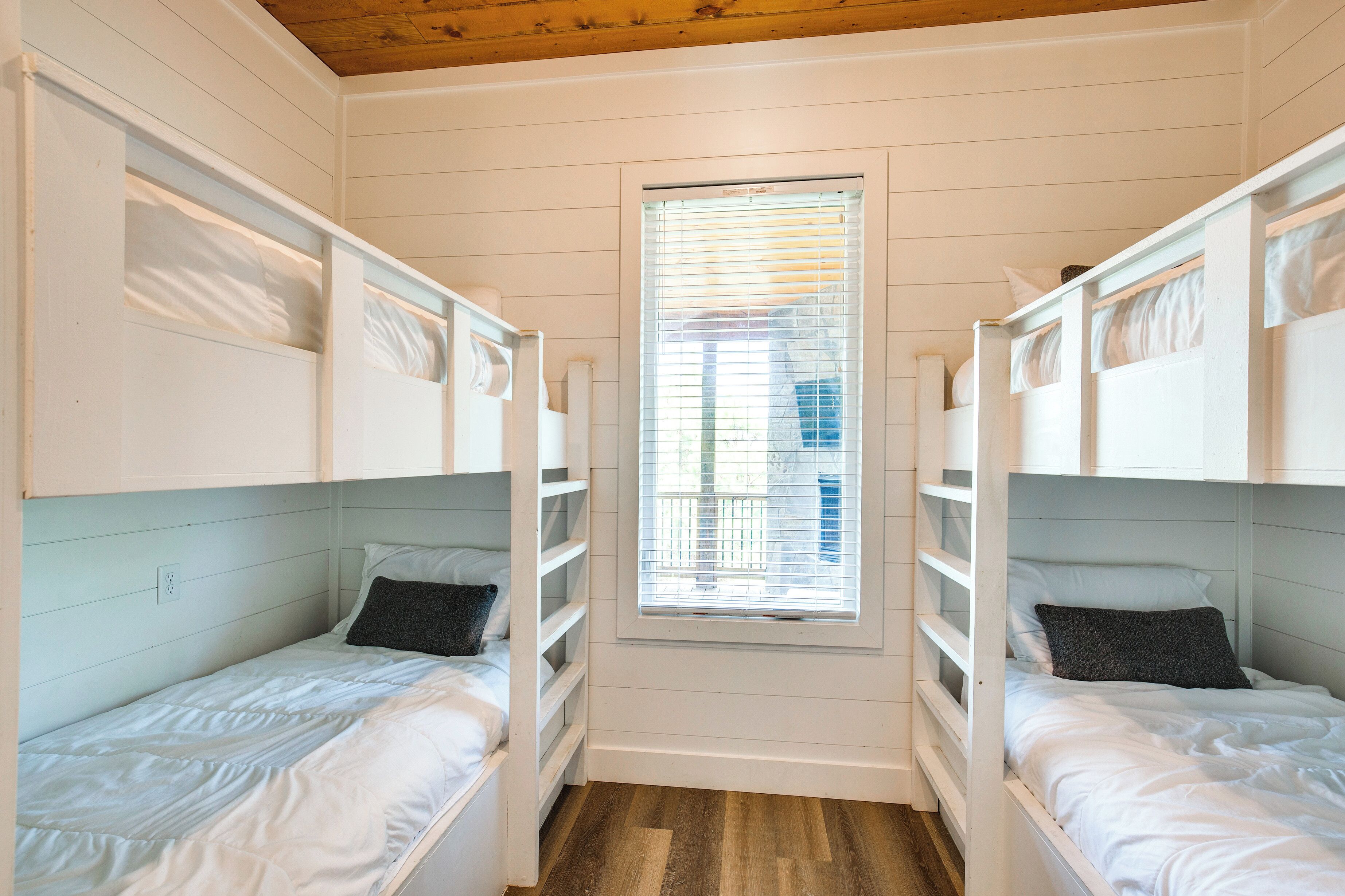 Una habitación con dos literas, una ventana con persianas y suelo de madera.