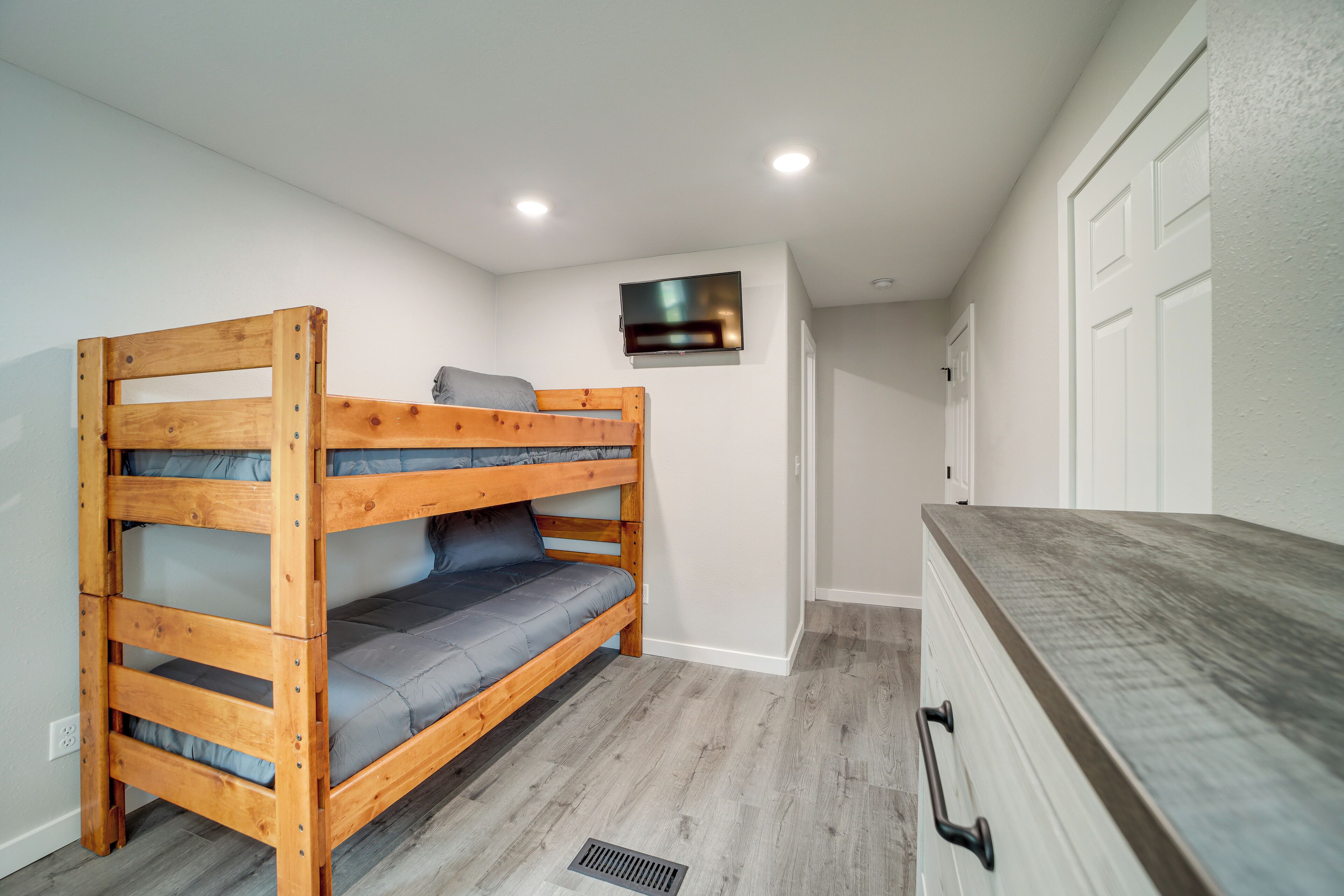 A bunk bed with a TV mounted on the wall above it, a dresser with drawers, and a door in the background.