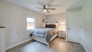 Une chambre à coucher comprenant un lit, une table de chevet, une lampe, un ventilateur de plafond et une porte.