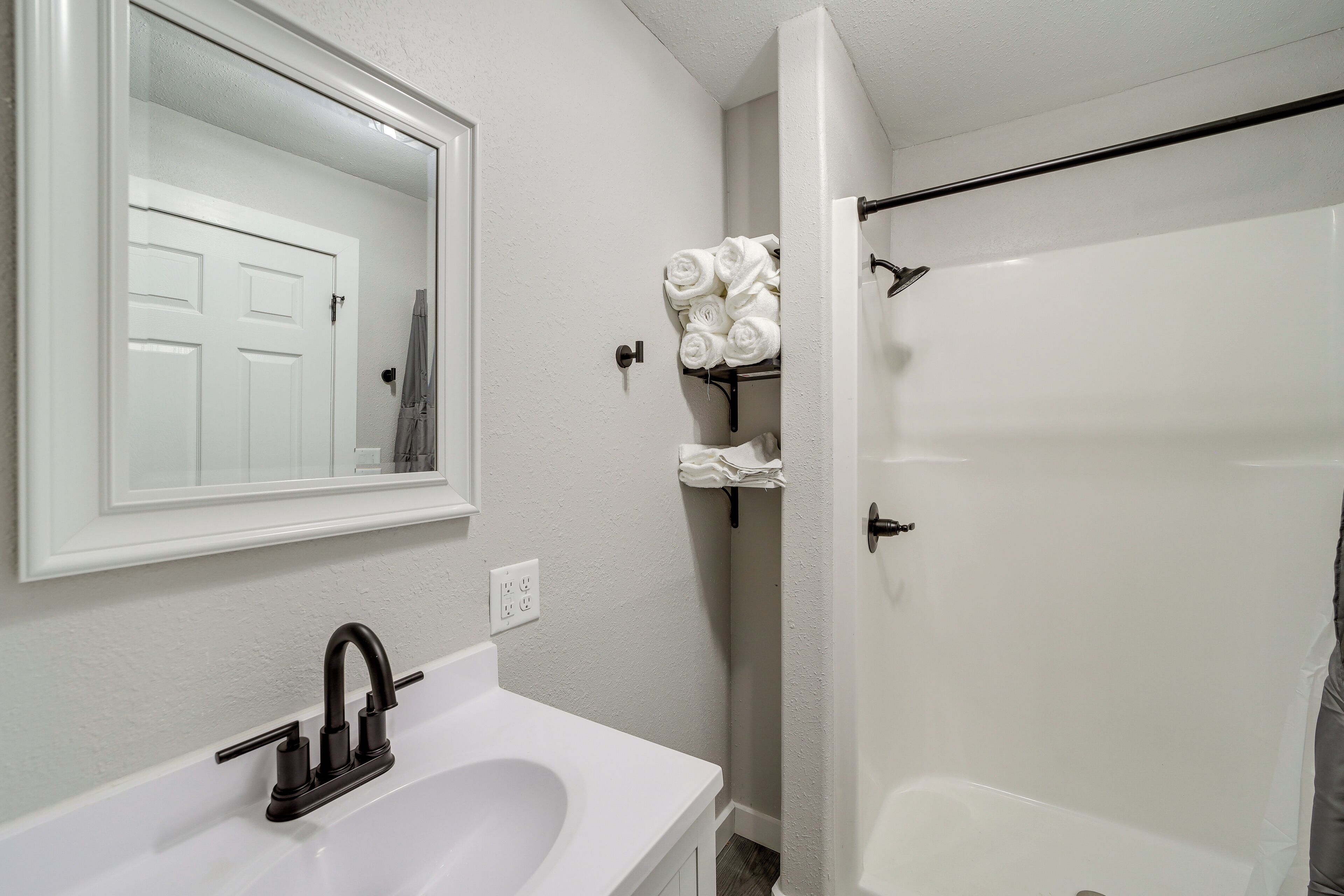 A bathroom with a white sink, a mirror, a shower, and a towel rack with towels.
