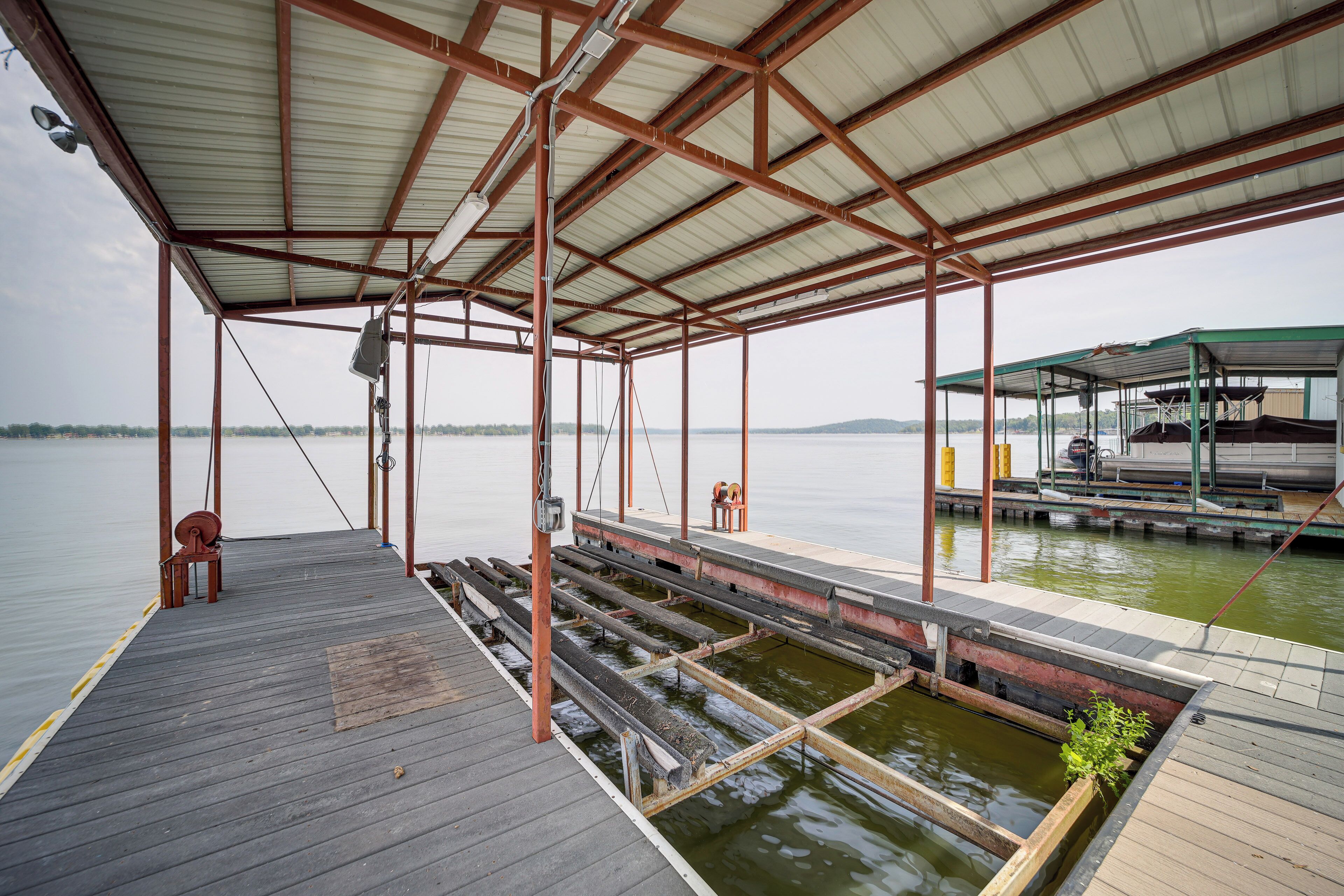 Un muelle techado con cubierta de madera, barandillas de metal y un pequeño banco.