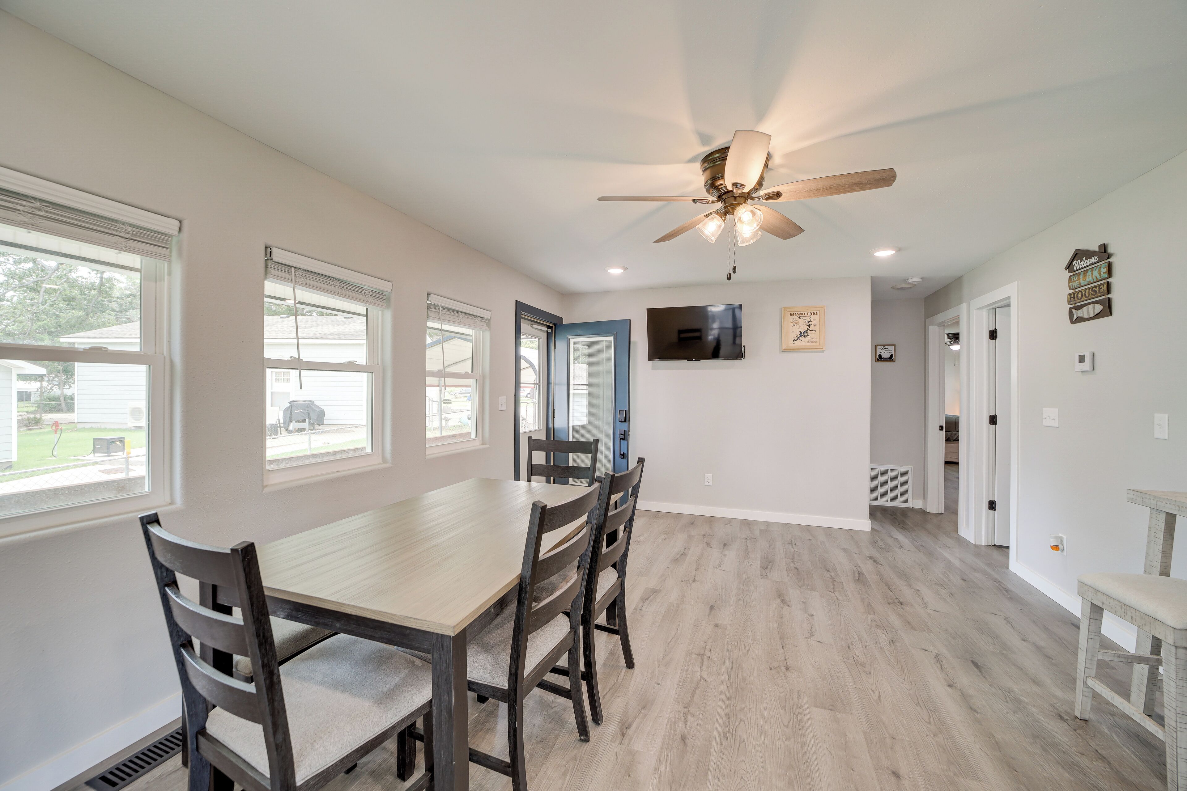 A spacious dining area with a wooden table and chairs, a ceiling fan, and large windows.
