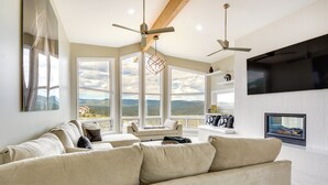 A spacious living room with a large beige sofa, a flat-screen TV mounted on the wall, and a view of the mountains through large windows. - Prescott Gem: Hot Tub & Mtn Views, 7 Mi to Dtwn (Prescott)