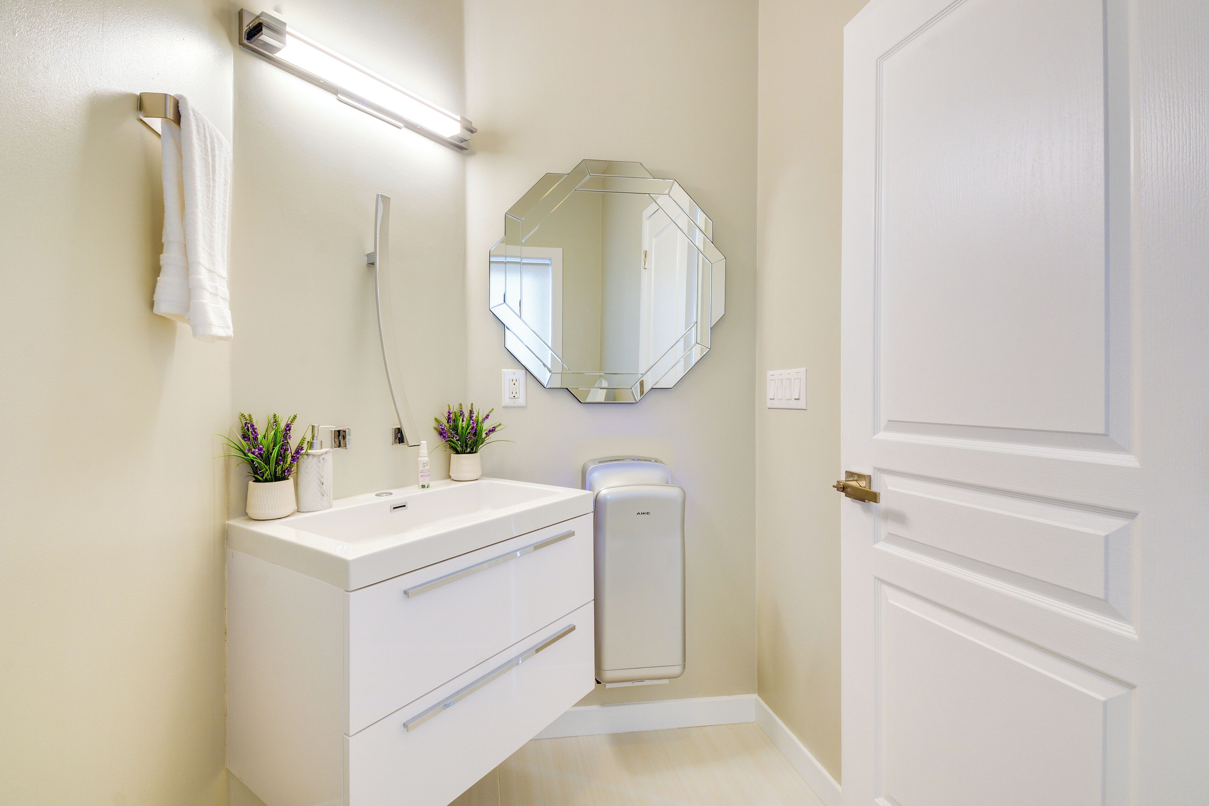 Une salle de bain moderne avec un meuble-lavabo blanc, un grand miroir et une porte.